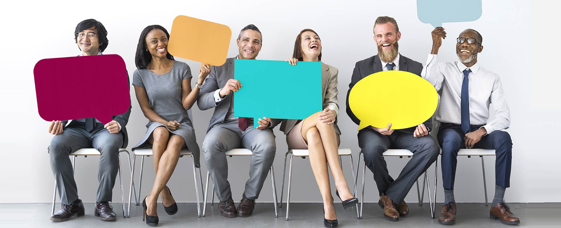 smiling-people-sitting-together-holding-up-blank-comment-bubble-cut-outs